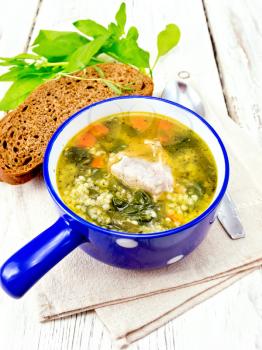 Pork ribs soup with couscous and spinach in a blue bowl on towel, bread on wooden board background