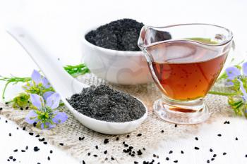 Flour Nigella sativa in a spoon, black cumin seeds in a bowl and oil in gravy boat on burlap, sprigs of kalingi with blue flowers and leaves on wooden board background