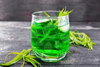 Tarragon lemonade with ice in a glass, estragon twigs on a wooden board background
