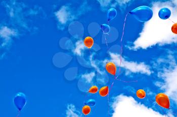 Orange and blue balloons against the sky and clouds