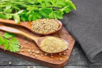 Coriander seeds and ground in two spoons, green fresh cilantro and a napkin on wooden board background
