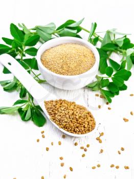 Fenugreek seeds in a spoon and ground spice in a bowl with leaves on wooden board background