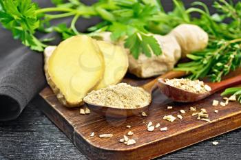 Ground ginger and flakes in two wooden spoons, ginger root, spicy herbs, napkin on a wooden board background