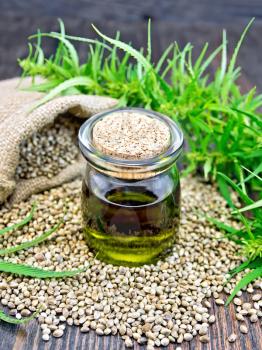 Hemp oil in a glass jar, grain in a bag and on the table, leaves and stalks of cannabis
on a wooden board background