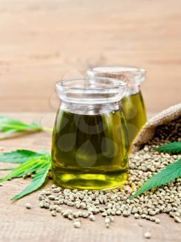 Hemp oil in two glass jars with grain in the bag and on the table, cannabis leaves on the background of wooden boards
