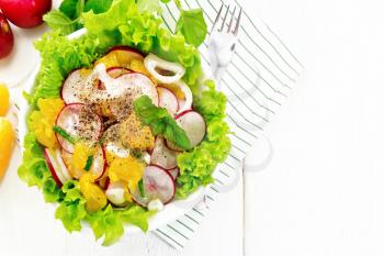 Radish, onion and orange salad with mint, vegetable oil and spices on lettuce in a plate on a towel on wooden board background from above