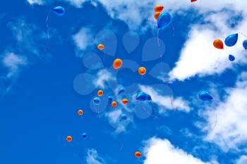 Orange and blue balloons against the sky and white clouds