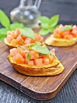 Bruschetta with tomatoes and basil, vegetable oil in a decanter on a wooden board background