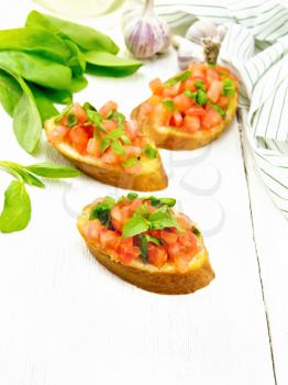 Bruschetta with tomato, basil and spinach, fresh spinach leaves, napkin, garlic and vegetable oil in decanter on wooden board background