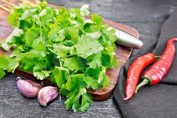Fresh cilantro, knife, garlic, hot red pepper and napkin against a black wooden board background