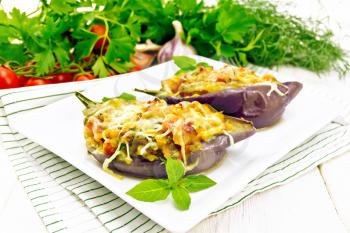 Stuffed eggplant with smoked brisket, tomatoes, onions, carrots with garlic, cheese and herbs in a plate on a napkin on white wooden board background