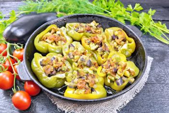 Sweet pepper stuffed with mushrooms, tomatoes, zucchini, eggplant and onions, seasoned with wine, garlic, thyme and spices in a frying pan on a napkin of sackcloth against dark wooden board
