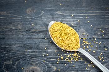 Mustard seeds in a metal spoon on the background of a black wooden board