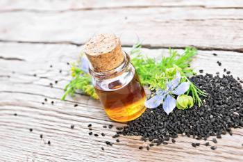 Nigella sativa oil in a bottle, seeds and sprigs of black cumin with blue flowers of kalingi on a background of an old wooden board