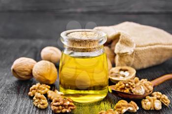 Walnut oil in a jar, nuts in a jute bag, in spoon and on table on wooden board background