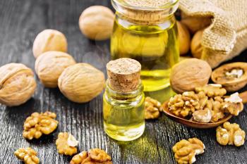 Walnut oil in a glass bottle and a jar, nuts in bag, spoon and on table on wooden board background
