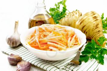 Salad of fresh carrots, parsnip and garlic with vegetable oil in a plate on napkin, fork, parsley and root vegetables on background of light wooden board