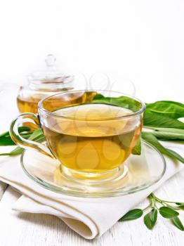 Herbal tea with sage in a glass cup and teapot on a napkin on wooden board background