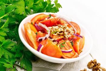 Fresh tomato salad with walnuts and red onions, seasoned with olive oil, vinegar, fenugreek and salt in a plate on a napkin on white wooden board background