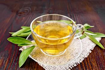 Herbal tea with sage in a glass cup on a burlap napkin on a wooden board background
