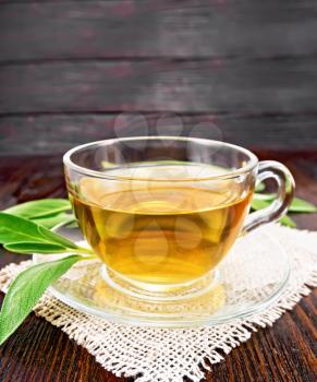 Herbal tea with sage in a glass cup on burlap on wooden board background