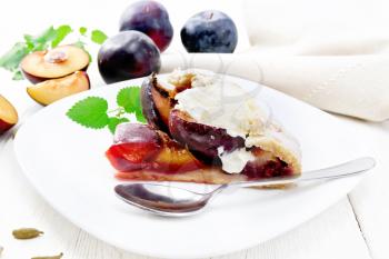 Piece of sweet pie with plum, sugar, cardamom and ice cream in a plate, sprigs of green mint, towel on light wooden board background