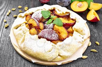 Sweet pie with plum, sugar and cardamom on parchment, sprigs of green mint on a dark wooden board background