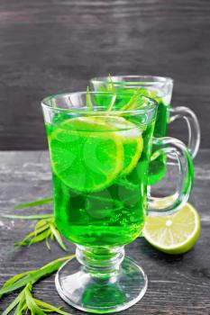 Tarragon lemonade with estragon sprigs, ice and lime slices in two goblets on a wooden board background