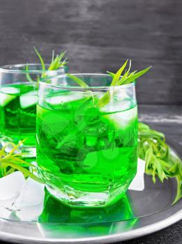 Tarkhun lemonade with ice in two glasses on a silver tray on black wooden board background