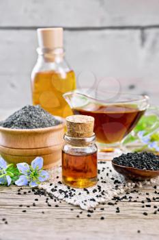 Nigella sativa oil in vial, gravy boat and bottle, seeds in a spoon and black cumin flour in a bowl on burlap, kalingi twigs with blue flowers and leaves on wooden board background