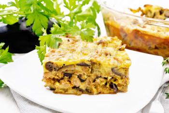 Casserole of minced meat, onion and eggplant, doused with a sauce of eggs, milk, cheese and flour in a plate on towel against white wooden board background