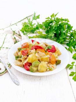 Vegetable ragout with zucchini, cabbage, potatoes, tomatoes and bell peppers in creamy sauce in plate, napkin, parsley and a fork on wooden board background