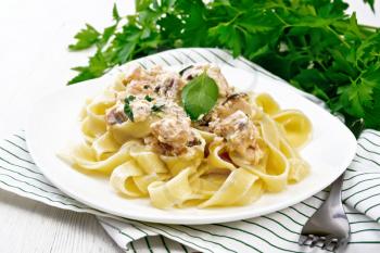 Tagliatelle pasta with salmon, cream, garlic and herbs in a plate on a kitchen towel, fork, parsley and basil on light wooden board background