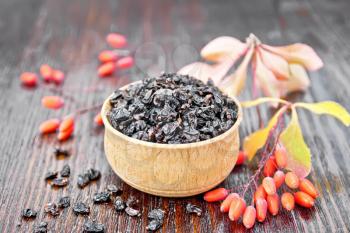 Dried black barberry in a bowl, sprigs with fresh berries and leaves on wooden board background