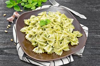 Farfalle pasta with pesto, basil in a plate on a towel against dark wooden board