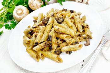 Penne pasta with wild mushrooms in a plate, towel, parsley and fork on a light wooden board background