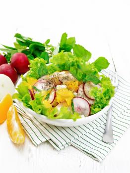 Radish, onion and orange salad with mint, vegetable oil and spices on lettuce in a plate on a striped napkin on wooden board background
