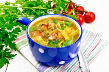 Soup with meat, tomatoes, vegetables, mung bean lentils and noodles in a blue bowl on towel, parsley and a spoon on wooden board background