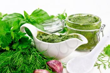Sauce of dill, parsley, basil, cilantro, other spicy herbs, garlic and vegetable oil in a gravy boat and a glass jar, a spoon with coarse salt on wooden board background
