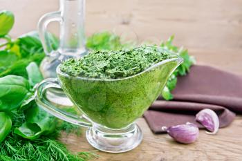 Sauce of dill, parsley, basil, cilantro, other spicy herbs, garlic and vegetable oil in a glass gravy boat, a towel on wooden board background
