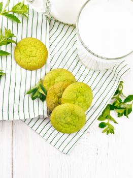 Green mint cookies on a towel with milk in a glass on the background of light wooden board from above