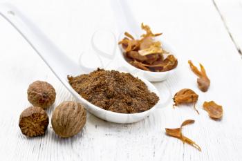 Ground nutmeg and dried nutmeg arillus  in two spoons, whole nuts on a white wooden board background