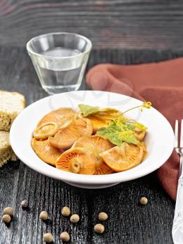 Salted mushrooms saffron with sour cream, currant leaf and sprig of dill in plate, fork, towel, bread and a glass of vodka on wooden board background