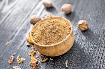Ground nutmeg in a bowl, whole nuts and dried nutmeg arillus on a dark wooden board background