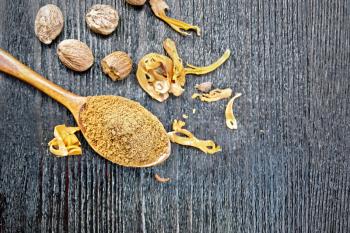 Ground nutmeg in a spoon, whole nuts and dried nutmeg arillus on a wooden board background from above