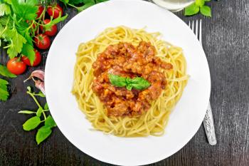 Spaghetti pasta with Bolognese sauce of minced meat, tomato juice, garlic, wine and spices in a plate, vegetable oil, spicy herb on a wooden board background from above
