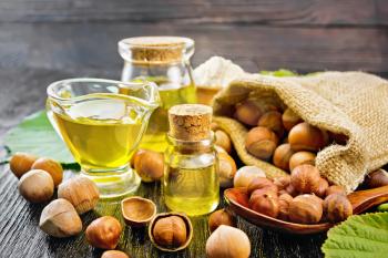 Hazelnut oil in a glass bottle, jar and gravy boat, flour in a bowl, nuts in bag, spoon and on the table, filbert sprigs with green leaves on wooden board background