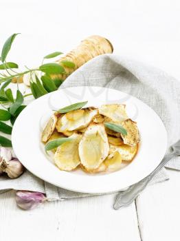 Baked parsnips with spices, garlic and sage in a plate on a towel on wooden board background