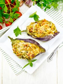 Stuffed eggplants with smoked brisket, tomatoes, onions, carrots with garlic, cheese and herbs in a plate on a kitchen towel on wooden board background from above