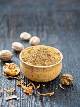 Ground nutmeg in a bowl, dried nutmeg arillus, whole nuts on a dark wooden board background